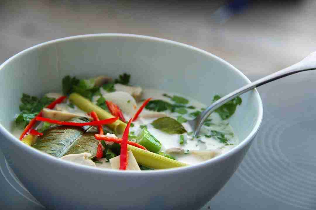 recette d'été rafraichissante : bol de soupe thai tom kha gai avec feuilles de kafir lime et batons de citronnelle