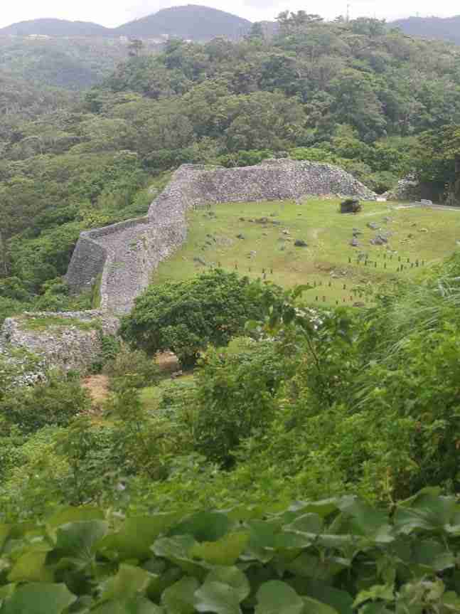 Okinawa : ruines du chateau de Nakijin : bout de muraille en forme d'étoile et herbes avec vestiges en pierre.